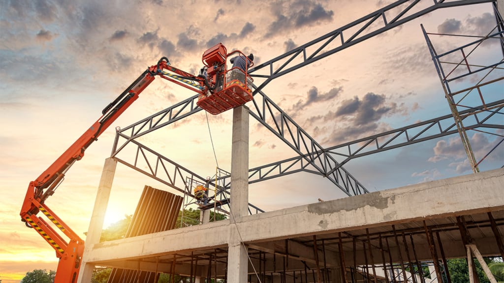Two construction workers are working on a building at sunset.