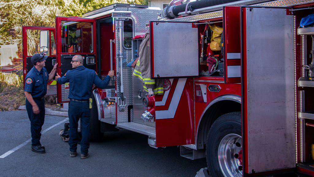 Two firefighters standing next to a fire truck.