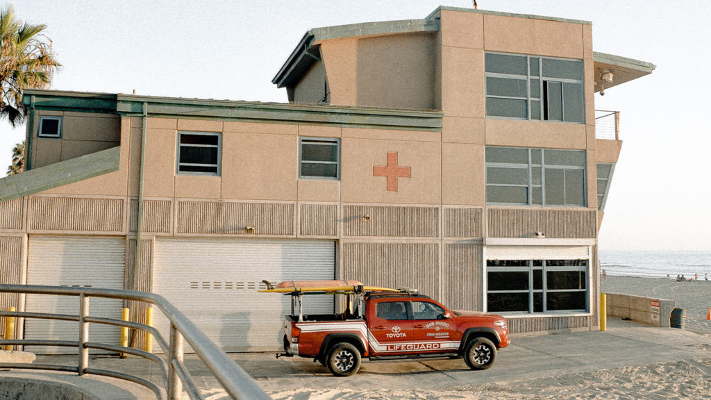 A red truck parked in front of a lifeguard building.