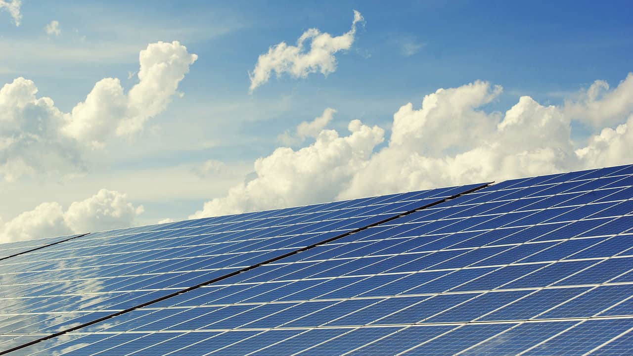 Solar panels under a partly cloudy sky, reflecting sunlight.