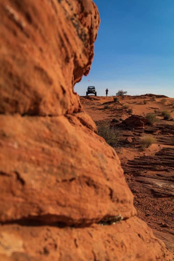 A UTV and driver in the distance by a cliff in the foreground.